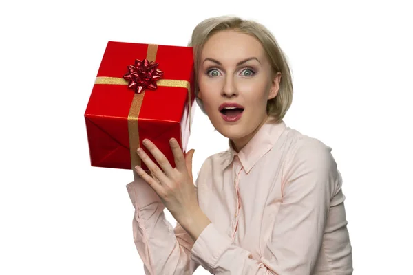 Mulher surpreendida com a boca aberta colocando sua orelha para o presente em papel vermelho . — Fotografia de Stock