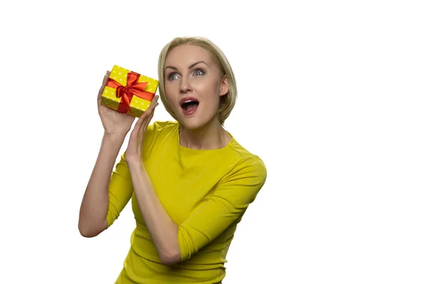 Felice eccitato giovane donna che tiene piccola scatola regalo gialla su orecchio isolato su sfondo bianco. — Foto Stock