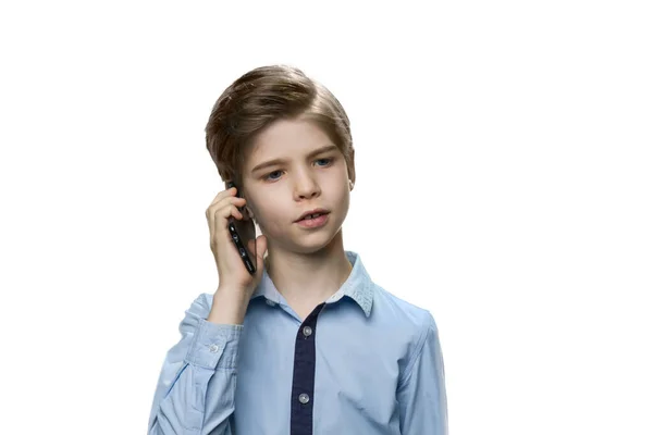 Chłopiec mówi na smartfonie w niebieskiej koszuli na białym tle. — Zdjęcie stockowe