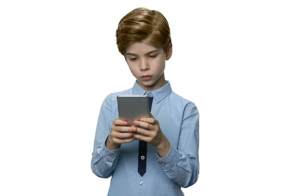 Chłopiec w niebieskiej koszulce z entuzjazmem patrzy na smartfona. — Zdjęcie stockowe