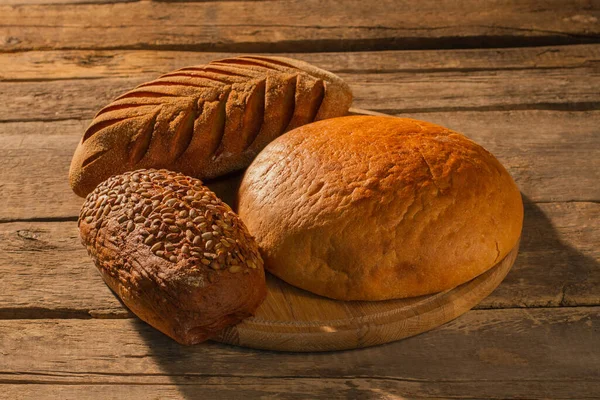 Drei Laibe selbstgebackenes Brot auf Schneidebrett. — Stockfoto