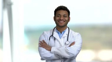 Mutlu genç doktor bulanık arka planda kollarını kavuşturdu..