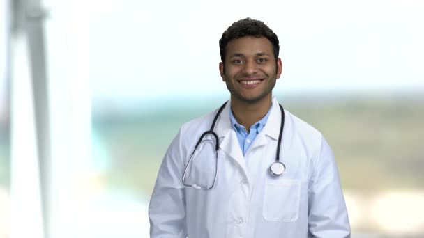 Knappe arts kijkt naar camera op wazige achtergrond. — Stockvideo