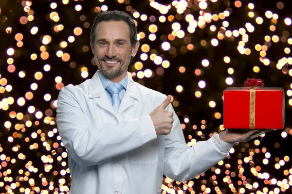 Handsome man in white coat holding gift box. — Stock Photo, Image