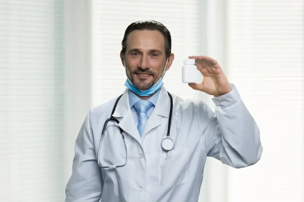 Professional male doctor showing bottle of pills.