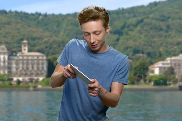 Teen boy playing mobile game on sea resort background.