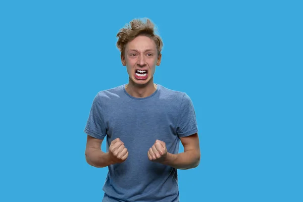 Crazy irritated teen boy is shouting on blue background. — Stock Photo, Image