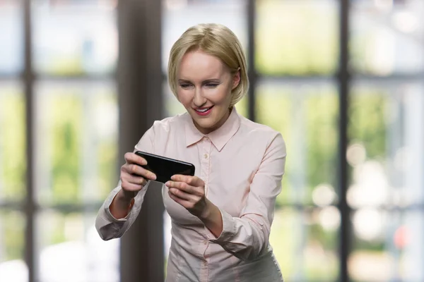 Funny blonde woman plays on her smartphone.