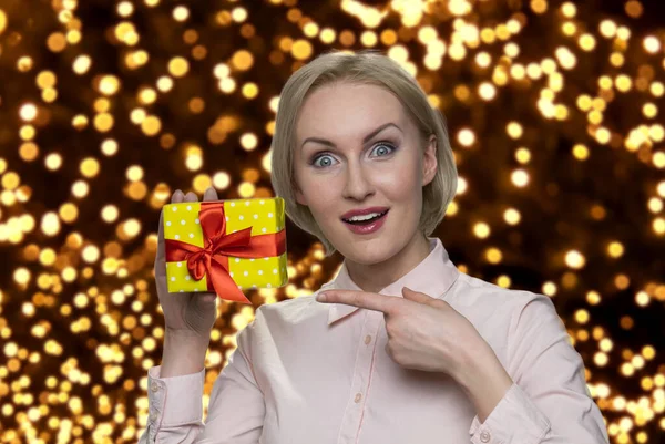 Glücklich geschockte Frau zeigt auf Geschenkbox. — Stockfoto