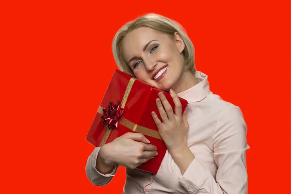 Mujer feliz abrazando caja de regalo sobre fondo rojo. — Foto de Stock