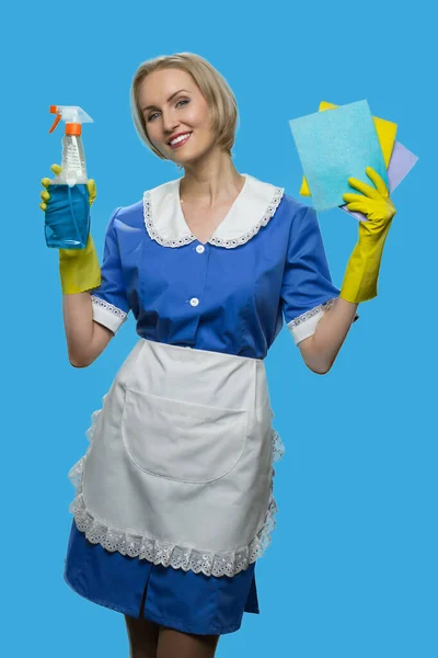 Cheerful maid in uniform holding rags and detergent. — Stock Photo, Image