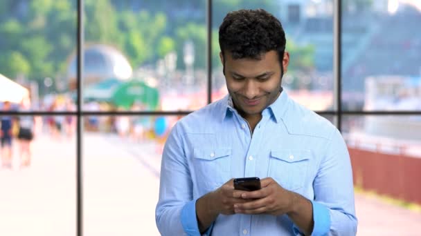 Jonge glimlachende man typt bericht op zijn telefoon. — Stockvideo