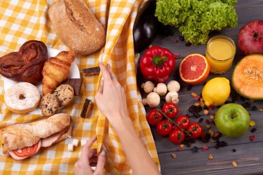 Kadın, sağlıksız yiyeceklerle bir masa örtüsünü yuvarlıyor..