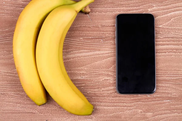 Dwa banany i smartfon na drewnie. — Zdjęcie stockowe