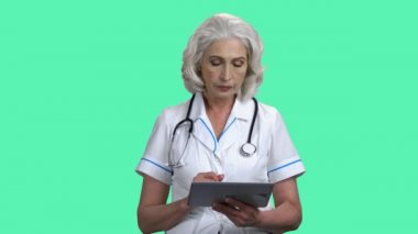 Olgun kadın doktor renk arkaplan üzerinde pc tableti kullanıyor.