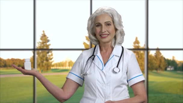 Smiling mature doctor presenting pills. — Stock Video