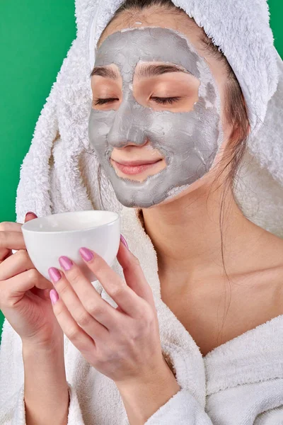 Close-up portret meisje met klei gezicht masker genieten van thee. — Stockfoto