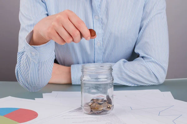 Крупним планом бізнес-леді кладе монету в скляну банку, щоб заощадити гроші . — стокове фото