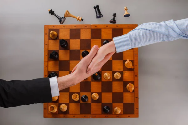 Biznesmen i kobieta ściskający dłonie nad szachownicą. — Zdjęcie stockowe