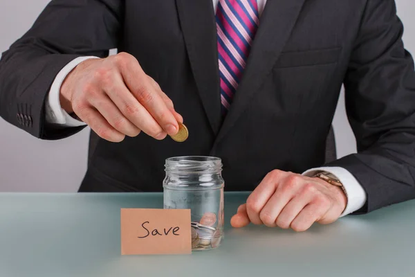 Man hand sätta mynt i glasburk för att spara pengar. — Stockfoto