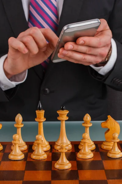 Businessman with smartphone planning strategy with chess figuures on table.