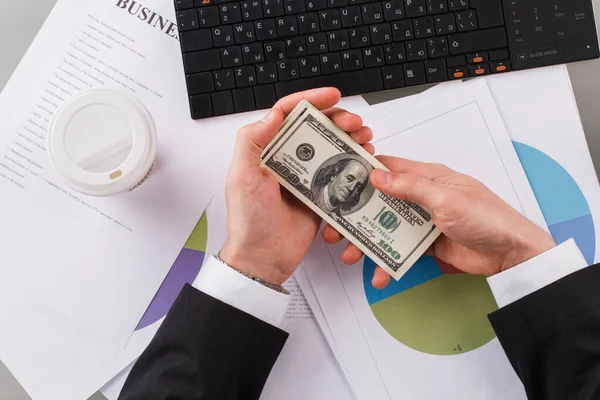 Empresario sosteniendo billetes de dólar cerca de la computadora en la mesa. — Foto de Stock