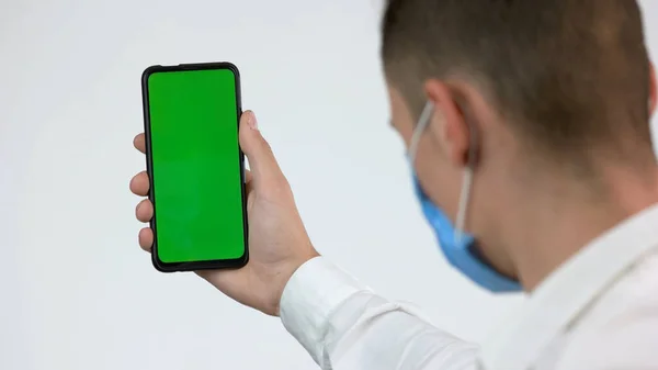 Mężczyzna w masce twarzy patrzy na zielony ekran telefonu. — Zdjęcie stockowe