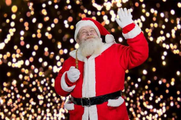 Weihnachtsmann winkt mit Hand auf Lichterhintergrund. — Stockfoto