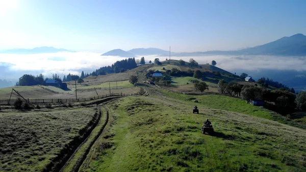 Quad ποδήλατα ιππεύει στους πράσινους λόφους προς το χωριό. — Φωτογραφία Αρχείου