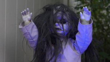 Soluk yüzlü, dağınık siyah saçlı ve el kaldıran ürkütücü bir Cadılar Bayramı bebeğinin yakın çekimi. Ürkütücü bahçe dekorasyonu sonbaharda perili bir korku ortamı yaratıyor..