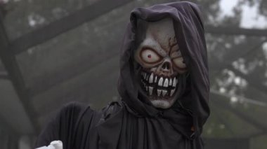 Kafatası yüzlü ve keskin dişli kapüşonlu Azrail pervanesinin yakın çekimi. Kırmızı parlayan gözler ve siyah bir pelerin dışarıda ürkütücü bir Cadılar Bayramı süsü oluşturur..