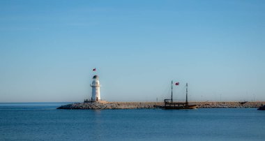 Limanın plajından panoramik manzara. Gün batımı güneşiyle aydınlatılan ışık evi.