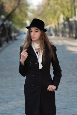 Siyah paltolu ve şapkalı şık bir kız caddede yürüyor. Şehir yaşam tarzı. Taze bahar çekimi