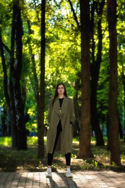 Şehir parkında yürüyen kendine güvenen bir kız. Gri paltolu genç bir kadın. Sokak yaşam tarzı