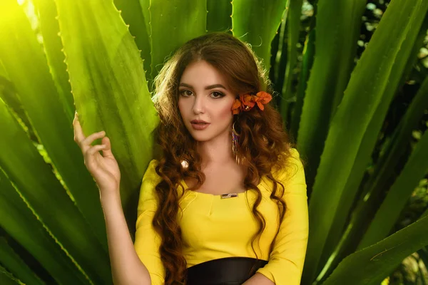 緑豊かな緑の木々の植物の間の庭に立って黄色の夏のドレスで美しい白人の若いモデルの女の子の肖像画 — ストック写真
