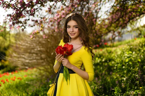 若いです美しいです女の子で黄色のドレス保持新鮮な春の花で庭 — ストック写真