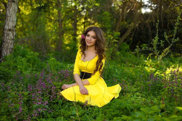 美しいです若いです女の子で黄色のドレスで草の上に春の庭に座って — ストック写真