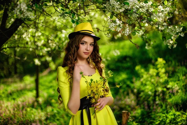 春に公園で黄色い帽子をかぶった幸せな十代の女の子 長いです巻き毛を身に着けている黄色のドレス — ストック写真