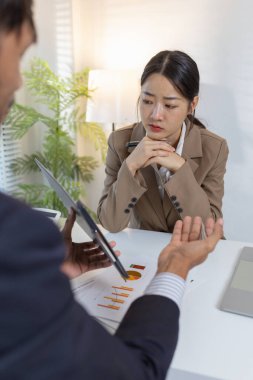 İki iş adamı modern bir ofiste finansal çizelge ve stratejileri tartışıyor. Resmi bir toplantıda fikir alışverişinde bulunur, raporları analiz eder ve çözümleri müzakere ederler..