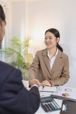 İş ortakları toplantılarını bir tokalaşma ile sonuçlandırır, güven, anlaşma ve başarılı işbirliğini sembolize eder. Çizelge ve raporları inceledikten sonra kararları doğrularlar..