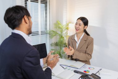 İki meslektaş başarılı tartışmayı neşeli ifadeler ve alkışlarla kutluyor. Olumlu etkileşimleri raporları inceledikten sonra takım çalışması, motivasyon ve memnuniyeti yansıtır..