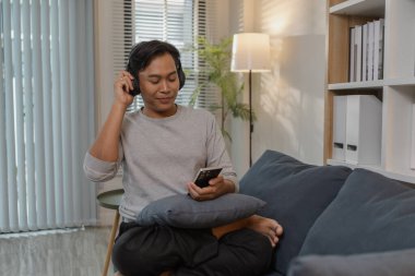 Genç bir adam evinde dinleniyor, kanepede keyfine bakıyor. Kulaklıkla müzik dinliyor, film izliyor ve şarkı söylüyor. Modern bir yaşam alanında mutluluk ve rahatlığı ifade ediyor..