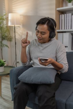 Genç bir adam evinde dinleniyor, kanepede keyfine bakıyor. Kulaklıkla müzik dinliyor, film izliyor ve şarkı söylüyor. Modern bir yaşam alanında mutluluk ve rahatlığı ifade ediyor..