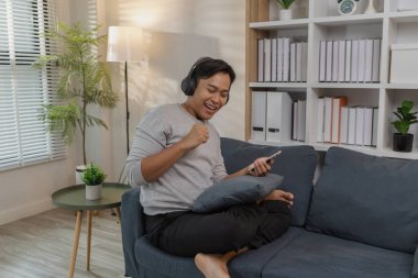 Genç bir adam evinde dinleniyor, kanepede keyfine bakıyor. Kulaklıkla müzik dinliyor, film izliyor ve şarkı söylüyor. Modern bir yaşam alanında mutluluk ve rahatlığı ifade ediyor..