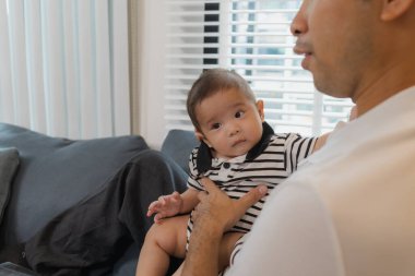 Bebeğini kucağında tutan bir babanın şefkatli anı. Bebek merakla ve güvenle yukarı bakıyor. Sıcak etkileşim aile sevgisini, yakınlaşmayı ve ebeveyn bakımını yansıtır..