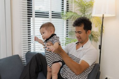 Bebeğini kucağında tutan bir babanın şefkatli anı. Bebek merakla ve güvenle yukarı bakıyor. Sıcak etkileşim aile sevgisini, yakınlaşmayı ve ebeveyn bakımını yansıtır..