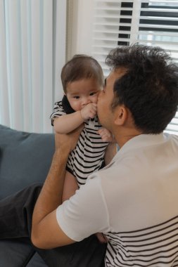 Bebeğini kucağında tutan bir babanın şefkatli anı. Bebek merakla ve güvenle yukarı bakıyor. Sıcak etkileşim aile sevgisini, yakınlaşmayı ve ebeveyn bakımını yansıtır..