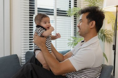 Bebeğini kucağında tutan bir babanın şefkatli anı. Bebek merakla ve güvenle yukarı bakıyor. Sıcak etkileşim aile sevgisini, yakınlaşmayı ve ebeveyn bakımını yansıtır..