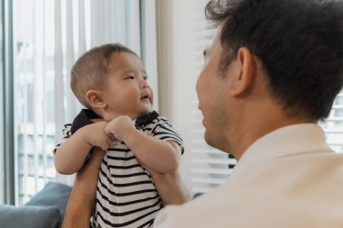 Bebeğini kucağında tutan bir babanın şefkatli anı. Bebek merakla ve güvenle yukarı bakıyor. Sıcak etkileşim aile sevgisini, yakınlaşmayı ve ebeveyn bakımını yansıtır..