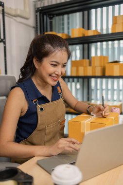 Genç bayan girişimci bir paket etiketinin üzerine bir nakliye adresi yazarak ev ofisine teslimat için bir paket hazırlıyor. Online bir iş yürütüyor ve müşterilere sevkiyat düzenliyor..